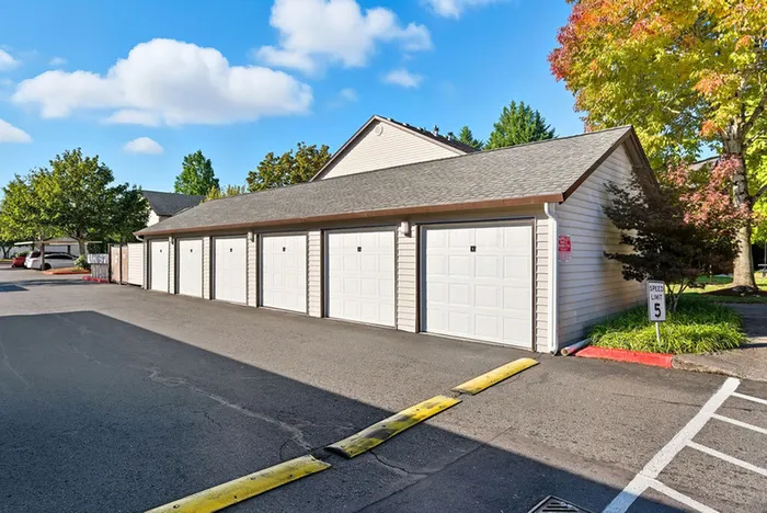 Charming apartment community with multiple garages, set amidst lush greenery and vibrant autumn foliage under a clear blue sky.