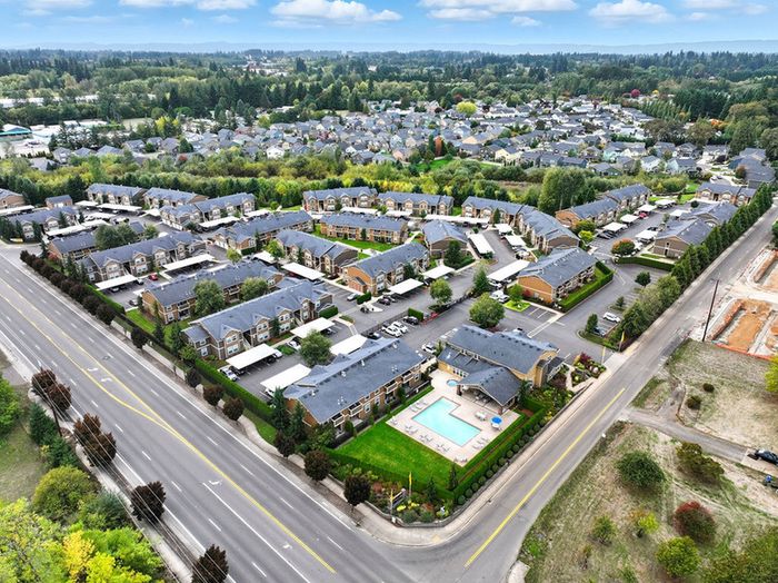 Breath-taking aerial view of an upscale apartment complex with lush greenery, outdoor pool, and ample parking, set in a vibrant and beautifully landscaped community.