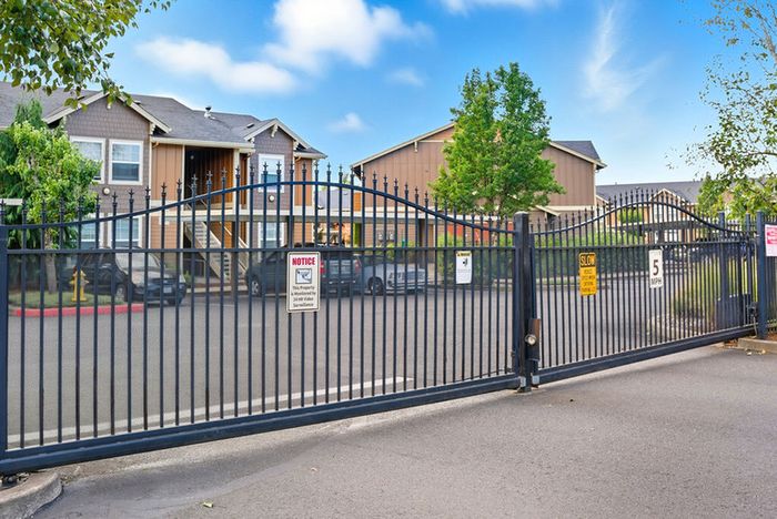 Secure gated entrance to a charming residential apartment community with lush greenery and convenient parking.