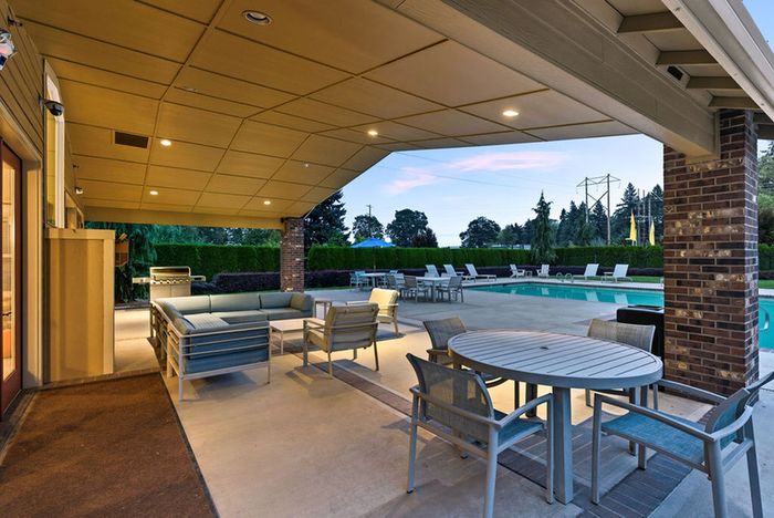 Chic outdoor seating area under a covered patio overlooking a sparkling pool, perfect for relaxing and entertaining.