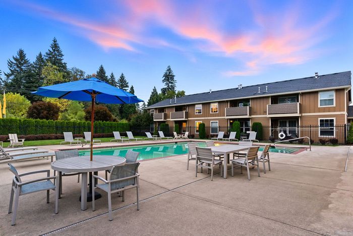 Inviting apartment complex with serene poolside seating, lush greenery, and vibrant sunset sky.
