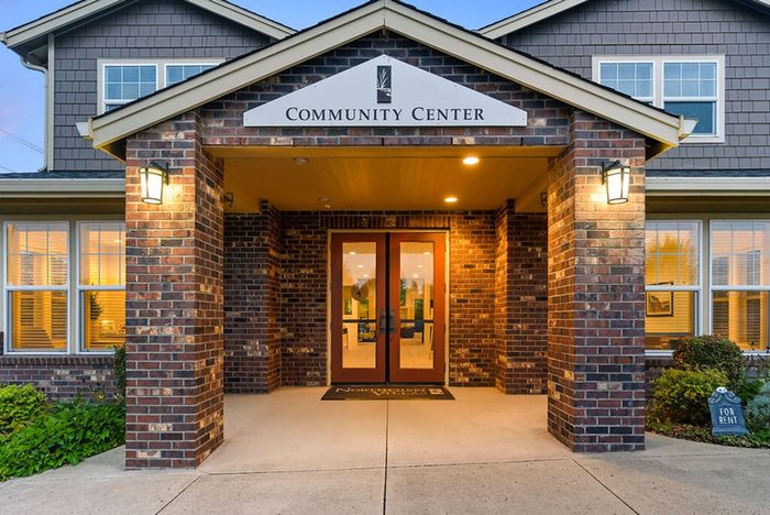Inviting community center entrance with warm brick facade and well-lit glass doors, welcoming ambiance for residents.