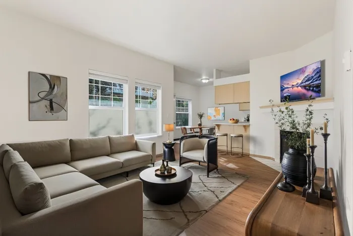 Contemporary living room featuring cozy beige sofas, modern decor, and a bright open layout leading to a kitchen with dining area.