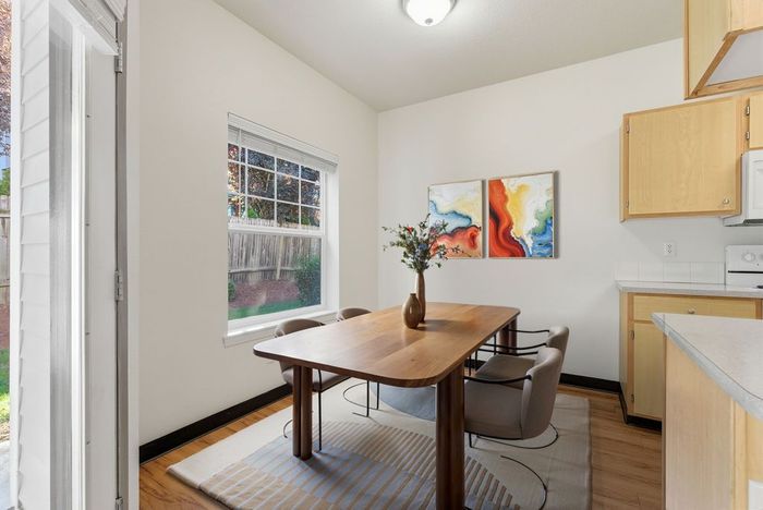 Bright dining area with a modern wooden table and chairs, featuring colorful abstract art and ample natural light from a large window overlooking a garden.