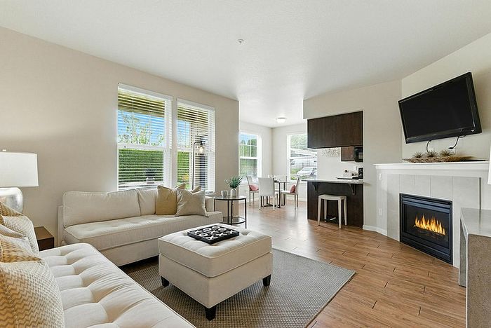 Bright and inviting living room with elegant fireplace, modern furnishings, and open kitchen in a stylish apartment setting.