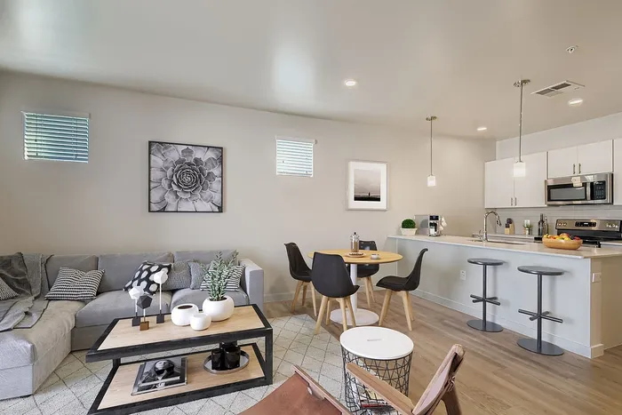 Modern living space with a cozy gray sofa, elegant coffee table, and a stylish open kitchen featuring a breakfast bar and sleek appliances.
