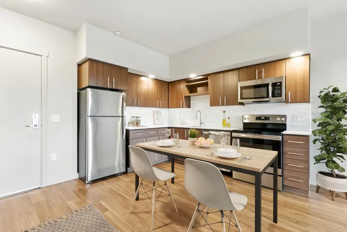 Modern kitchen with sleek stainless steel appliances, stylish wooden cabinetry, and a cozy dining area for two in a bright, inviting space.