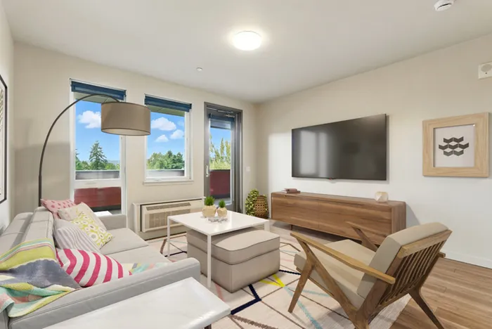 Bright and inviting living room with modern decor, featuring a cozy sofa, stylish armchair, and large wall-mounted TV, with expansive windows offering a view of lush greenery.