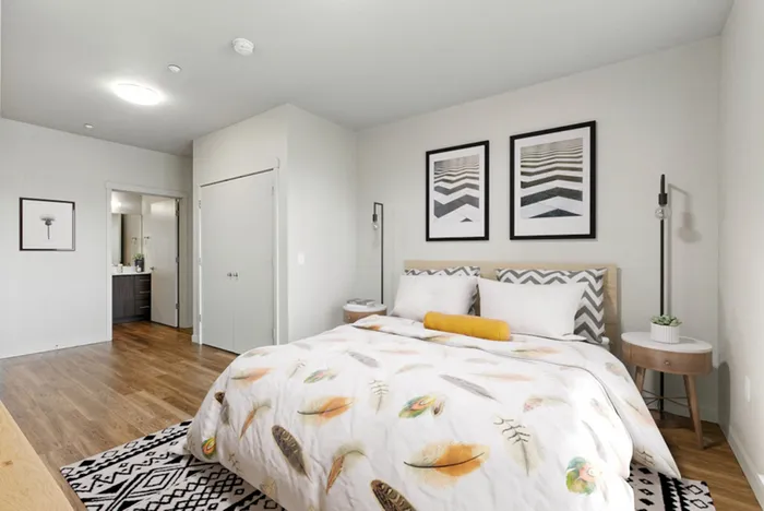Inviting bedroom with modern decor, hardwood floors, and en-suite bathroom. Features stylish artwork and cozy bedding for a serene retreat.