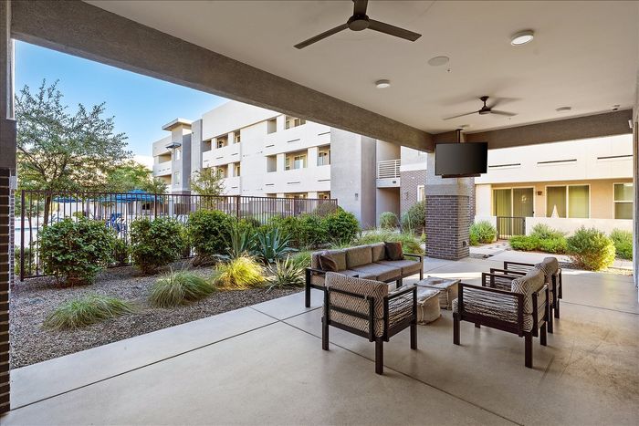 East Mesa, AZ, Pet-Friendly Apartments - Acero Eastmark - Covered Outdoor Lounge With Patio Seating, Ceiling Fans, Mounted Television, and Landscaped Courtyard Views.