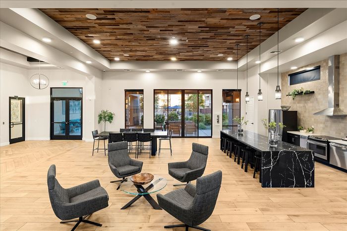 Modern open-concept living space featuring elegant wood panel ceiling, stylish gray seating area, sleek black marble kitchen island, and abundant natural light.