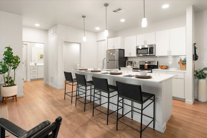 Modern kitchen with sleek white cabinetry, stainless steel appliances, and an inviting island breakfast bar with chic seating, set against warm wooden flooring.