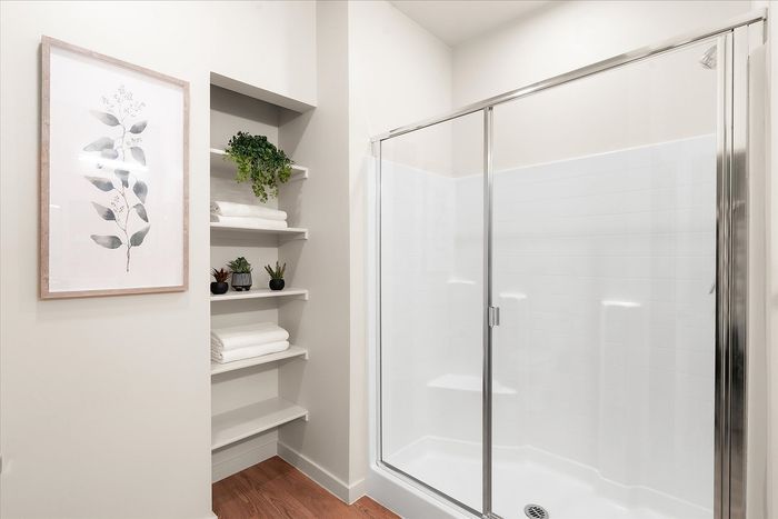 Elegant bathroom with modern glass shower, built-in shelves adorned with lush greenery and towels, and tasteful botanical wall art.