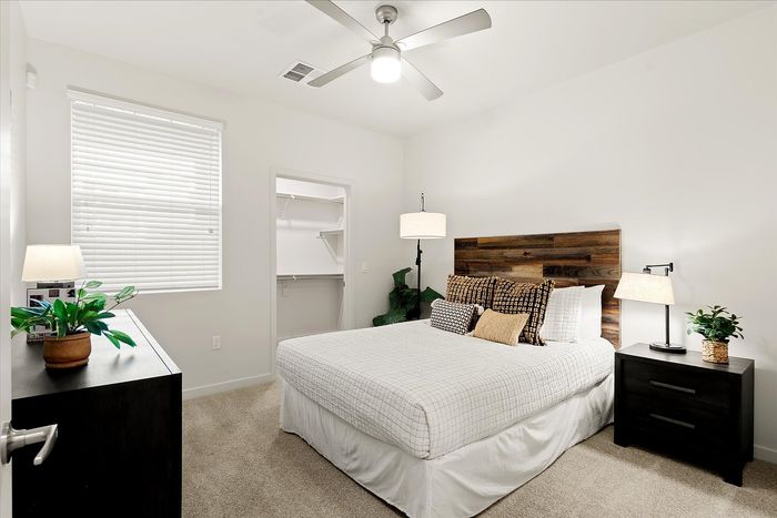 1-Bedroom Apartments in East Mesa, AZ - Acero Eastmark - Spacious Bedroom With Wood Headboard, Ceiling Fan, Window Blinds, Carpet Flooring, and Open Closet.