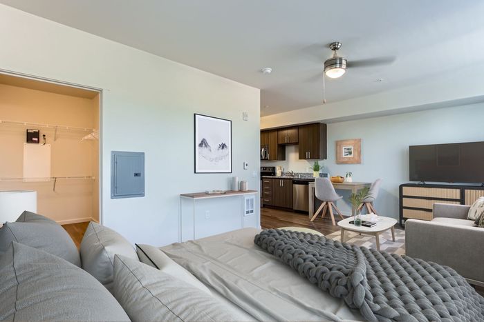 Modern open-plan living space featuring a cozy bedroom with plush bedding, a sleek kitchen with wooden cabinetry, and a stylish dining area with contemporary decor.