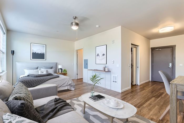 Elegant studio apartment featuring a cozy bed, stylish decor, and a bright open living space with hardwood floors.