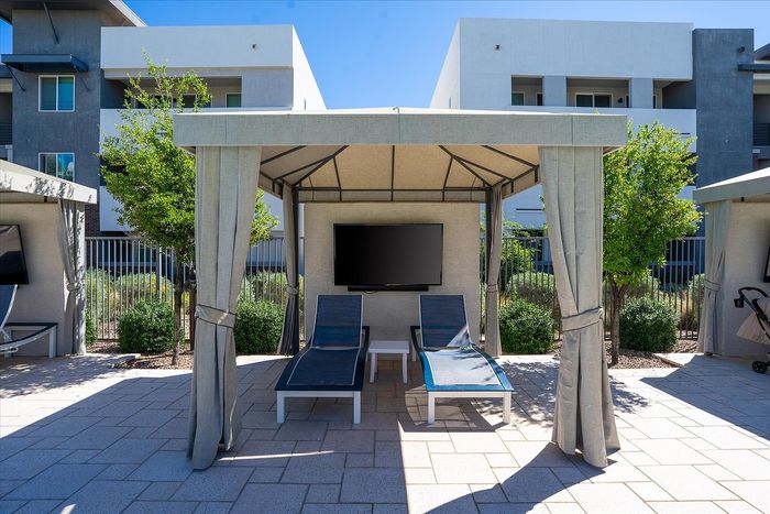 Inviting outdoor cabana featuring two modern lounge chairs, a flat-screen TV, and vibrant greenery, perfect for relaxation.