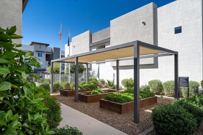 Modern apartment exterior showcasing a lush garden area with raised planters under a sleek canopy, perfect for residents seeking tranquility and style.
