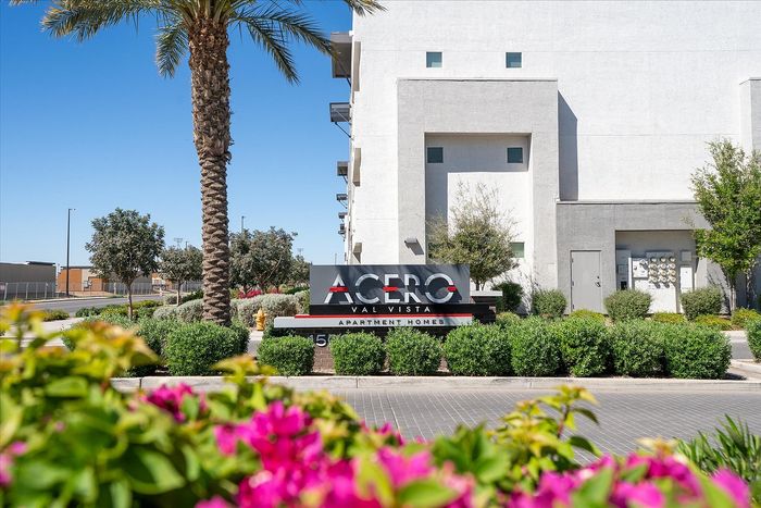 Charming Acero Val Vista Apartment Homes entrance with lush greenery and vibrant flowers in a serene neighborhood.