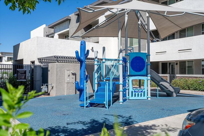 Modern apartment complex featuring a vibrant children's playground with slides and shade structures, surrounded by lush greenery.