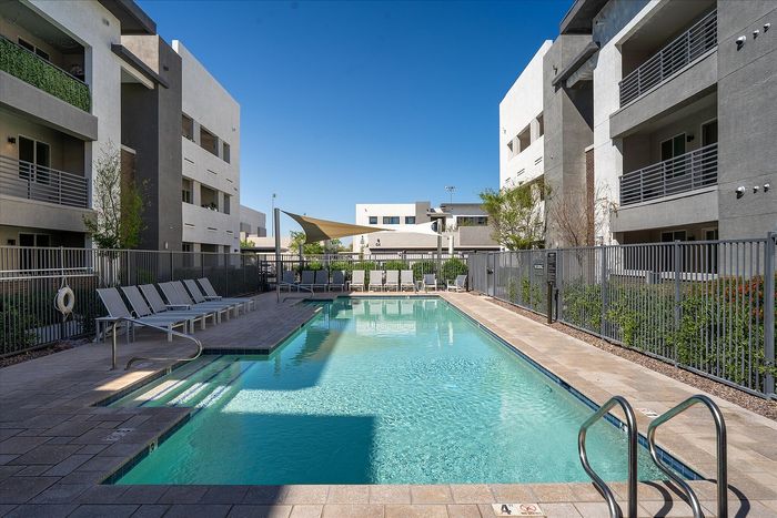 Modern apartment complex featuring a sparkling swimming pool, surrounded by sleek lounge chairs and shaded canopies, providing a luxurious and relaxing outdoor escape.