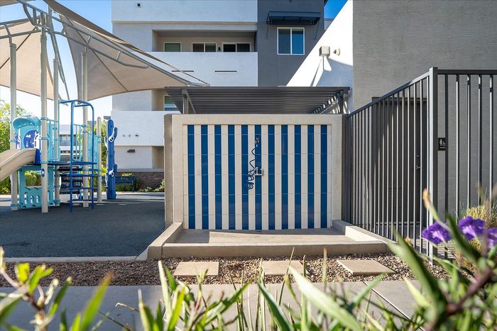 Modern apartment complex with shaded playground and striking blue striped wall, offering fun and relaxation for families.