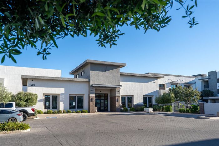 Contemporary apartment complex exterior with sleek architecture, ample parking, and lush landscaping under a clear blue sky.