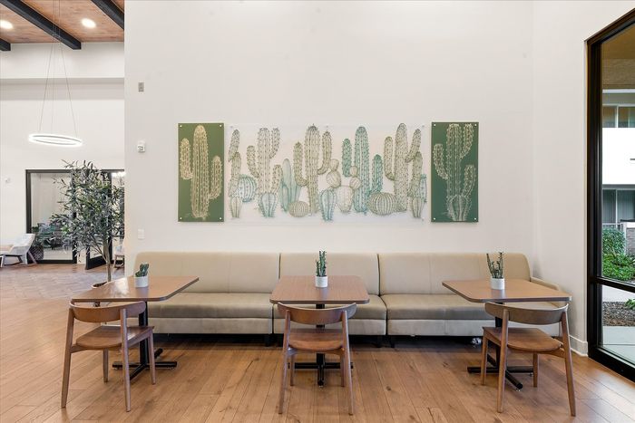 Chic and inviting dining area with modern decor, featuring cactus-themed artwork, cozy seating, and sleek wooden tables.