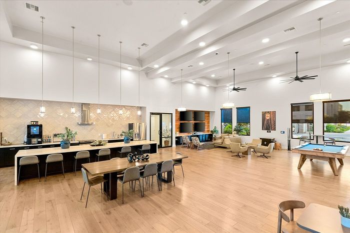 Spacious modern communal area featuring a sleek kitchen, elegant dining setup, cozy lounge chairs, and an entertaining pool table under vibrant lighting.