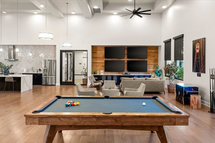 Modern open-concept living space featuring a sleek kitchen, stylish lounge area with multiple screens, and a classic billiards table for entertainment.