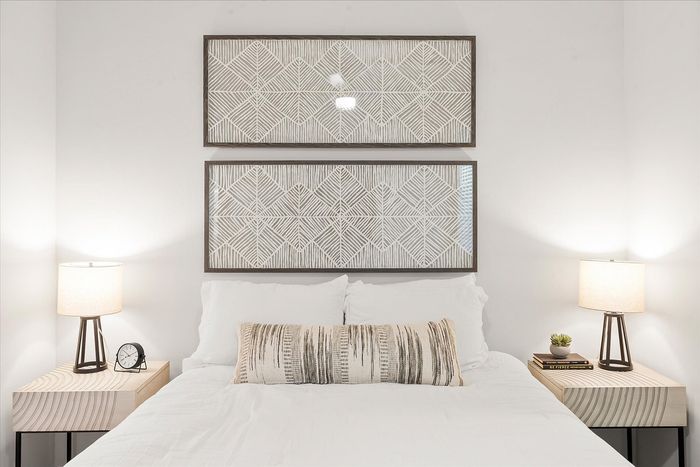 Elegant bedroom showcasing a modern bed with crisp white linens, flanked by stylish bedside tables with matching lamps, and adorned with sophisticated geometric wall art.