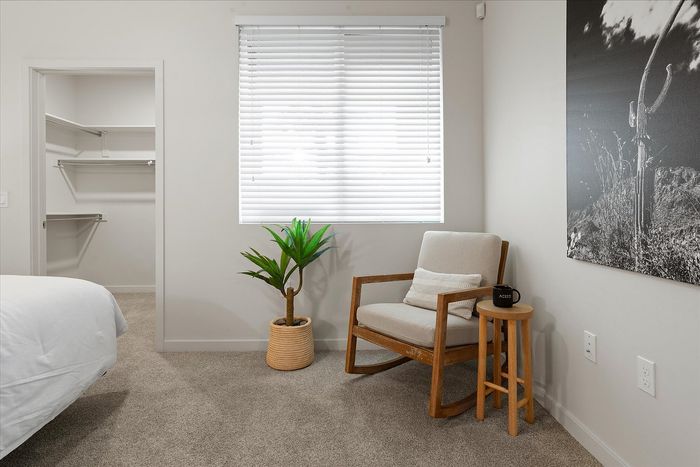 Chic bedroom corner featuring a cozy rocking chair, stylish plant, and an inviting open closet.