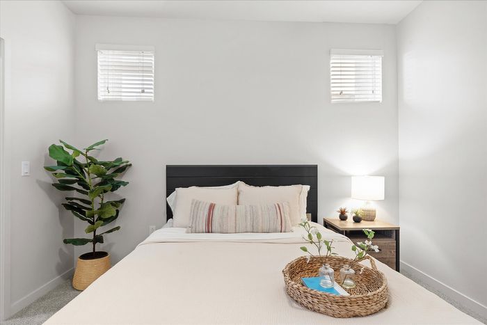 Serene bedroom with plush bedding, natural lighting, and stylish decor including a potted plant and cozy bedside lamp.