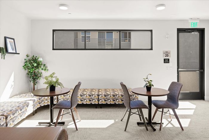 Modern lounge area with stylish decor, featuring two cozy seating arrangements, vibrant greenery, and large windows allowing natural light to fill the space.