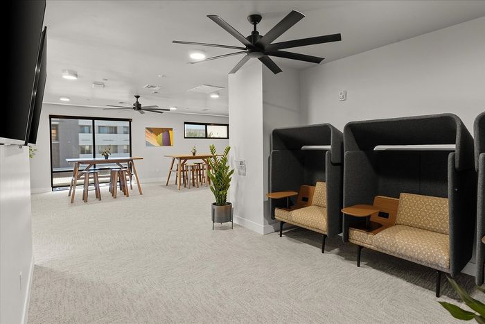 Modern communal workspace with stylish seating pods, sleek ceiling fans, and natural light from large windows.