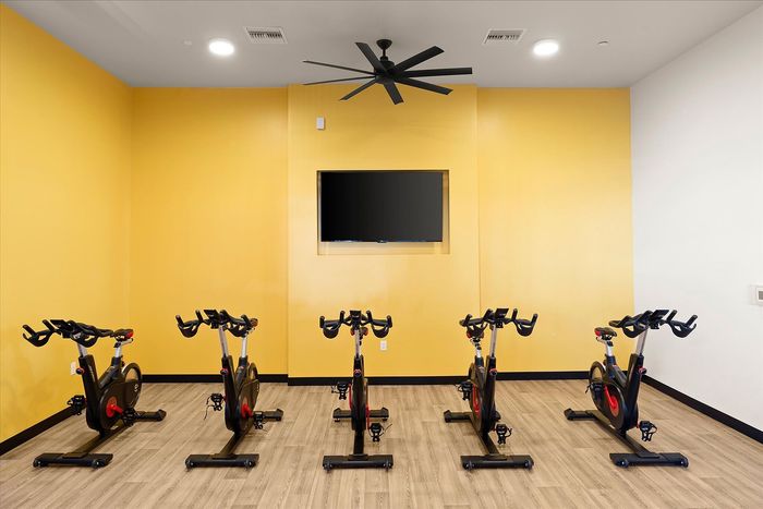 Modern indoor cycling studio with sleek stationary bikes, vibrant yellow accent wall, and mounted TV for entertainment.
