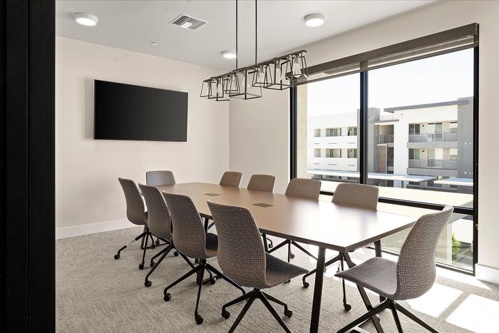 Modern conference room featuring a large table, comfortable chairs, and abundant natural light from floor-to-ceiling windows.