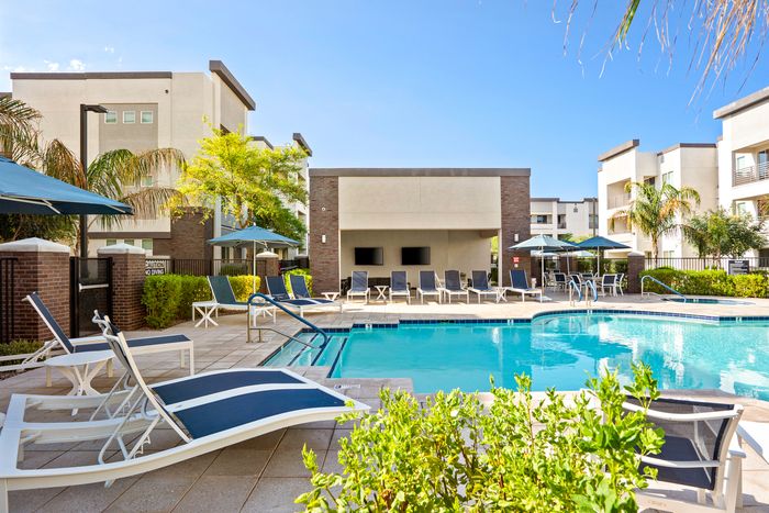 Chic apartment complex with a sparkling outdoor pool, surrounded by modern lounge chairs and lush greenery, perfect for relaxation.