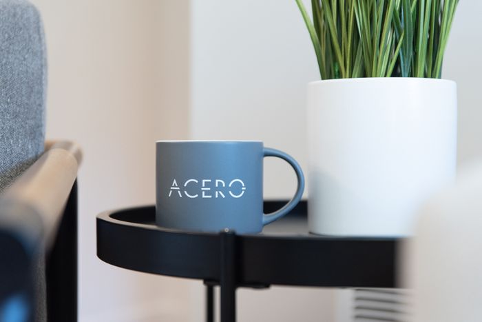 Chic interior detail with a cozy grey mug labeled 'ACERO' next to a vibrant green plant on a sleek black table.