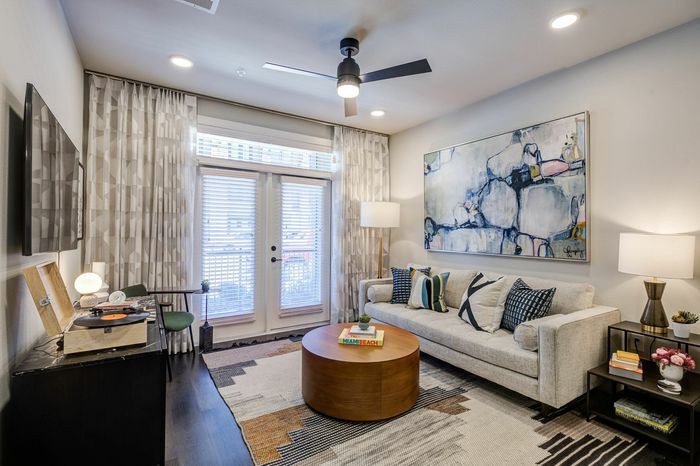 Inviting living room with modern decor, featuring a cozy sofa, sleek artwork, and a large window with natural light.