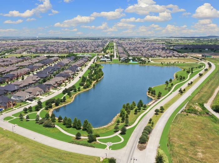 Scenic aerial view of a lakeside residential community with beautiful homes, lush greenery, and winding roads under a clear blue sky.