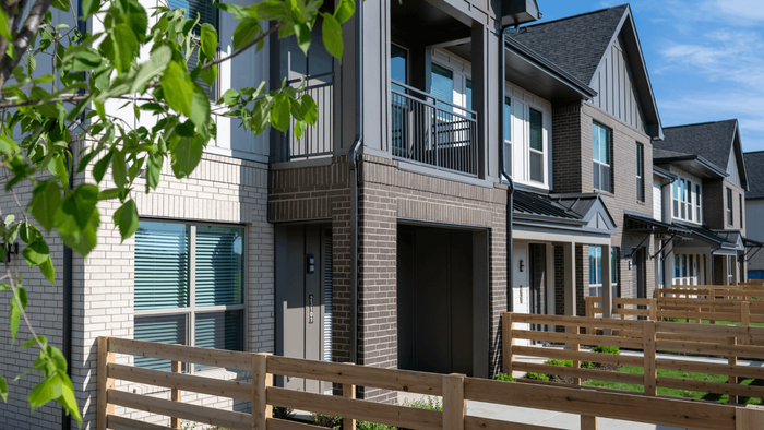 Modern townhouse complex with sleek design, featuring spacious balconies and charming wooden fences, surrounded by lush greenery.