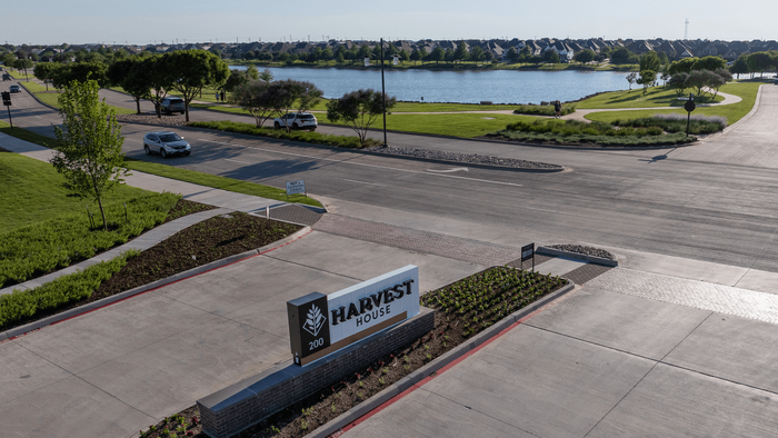 Scenic view of Harvest House entrance with lush greenery, spacious roads, and a tranquil lake in the background.