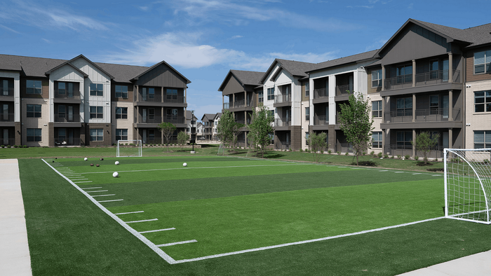 Modern apartment complex featuring stylish three-story buildings overlooking a lush green soccer field, perfect for outdoor activities and sports.