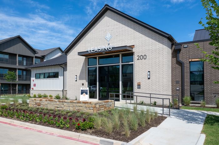 Chic leasing office entrance with modern architecture and vibrant landscaping under a clear blue sky.