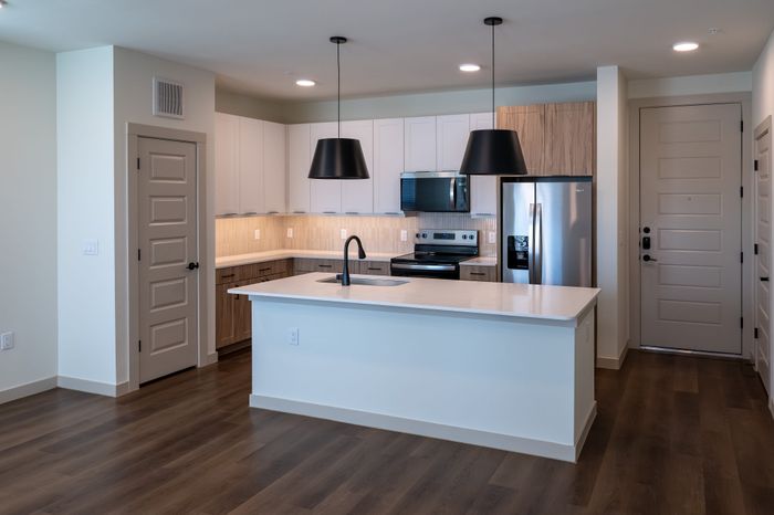 Modern kitchen featuring a sleek island with integrated sink, stainless steel appliances, and elegant pendant lighting. The hardwood floors and abundant cabinetry offer style and functionality.