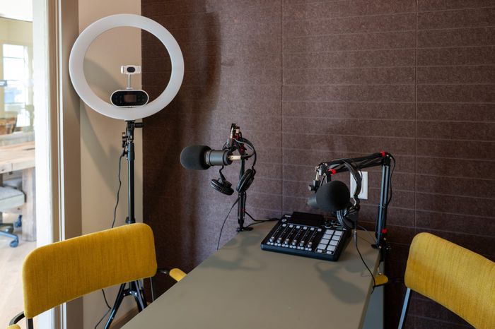 Modern podcast studio setup featuring professional microphones, headphones, and a ring light for optimal recording, complemented by vibrant yellow chairs and stylish wall paneling.