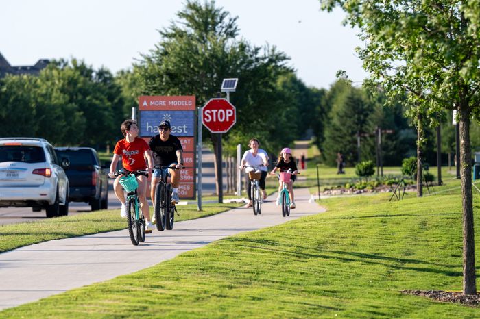 Lively community scene with people biking on a scenic pathway surrounded by lush greenery, evoking a vibrant outdoor lifestyle.
