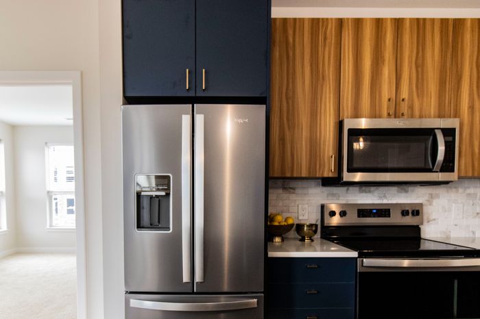 The James Apartments | Stainless Steel Modern kitchen with stainless steel appliances, including a double-door refrigerator and microwave, accented by dark blue and wooden cabinetry | Luxury Apartments in Haverhill MA