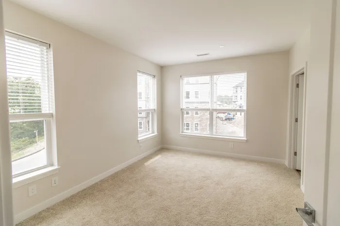 The James Apartments | Bright, empty bedroom with large windows, light-colored walls, and carpeted flooring, offering a spacious feel | Luxury Apartments in Haverhill MA